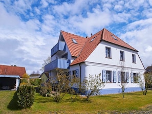 A two-story house with a red-tiled roof, a balcony on the upper floor, and a well-maintained lawn. - New Row 43 Villa Regulus Ground Floor (Zingst)
