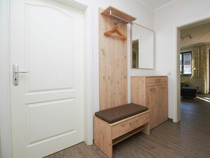 Una habitación con una puerta blanca, armario de madera, banco y espejo.