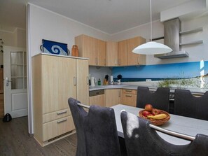 A modern kitchen with wooden cabinets, a dining table with chairs, and a view of the sea through a window. - New Row 43 Villa Regulus Ground Floor (Zingst)