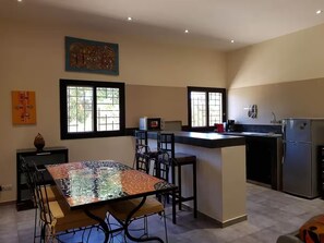 A modern kitchen with a dining area, featuring a central island, bar stools, and a refrigerator. - Villa Victoria Somone Senegal (Somone kanda)