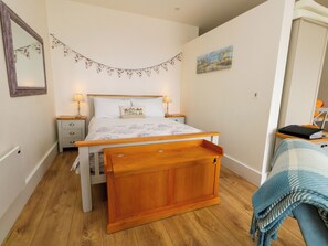 A bedroom with a wooden bed, bedside tables, a nightstand, a lamp, a wall-mounted mirror, a painting, and a window. - 4 The Beaches (Weymouth)