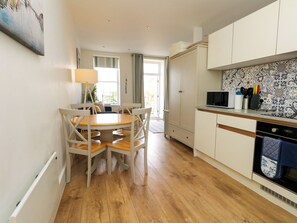 A modern kitchen with white cabinets, a wooden dining table, and a microwave. - 4 The Beaches (Weymouth)
