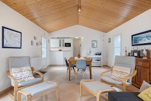 Una habitación amplia con techo de madera alto, un comedor con mesa y sillas, y una cocina al fondo.