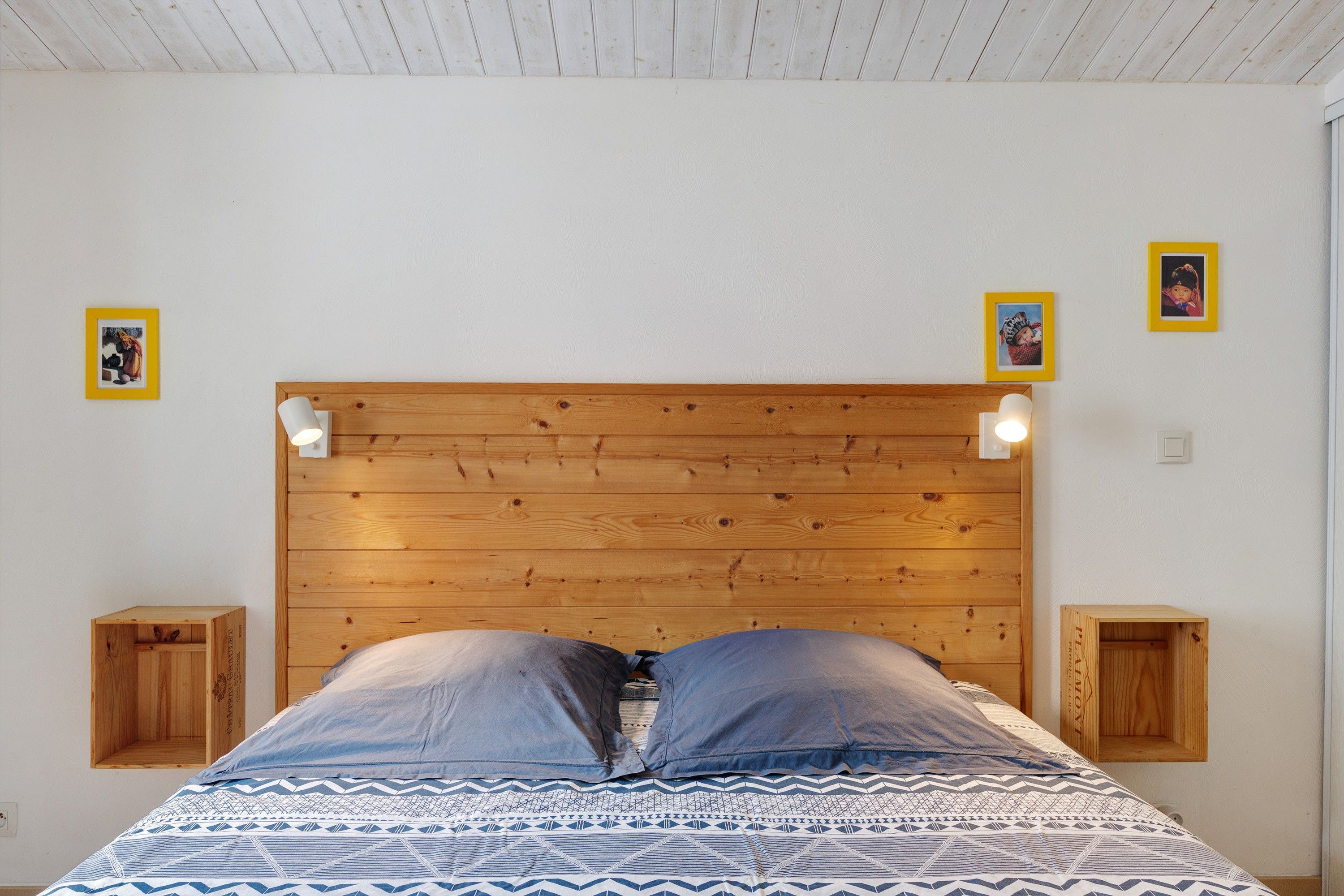 Un dormitorio con cabecera de madera, dos mesitas de noche, una colcha estampada y dos cuadros en la pared.