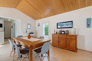 Un comedor con una mesa de madera, sillas y un mueble con dispositivos electrónicos.