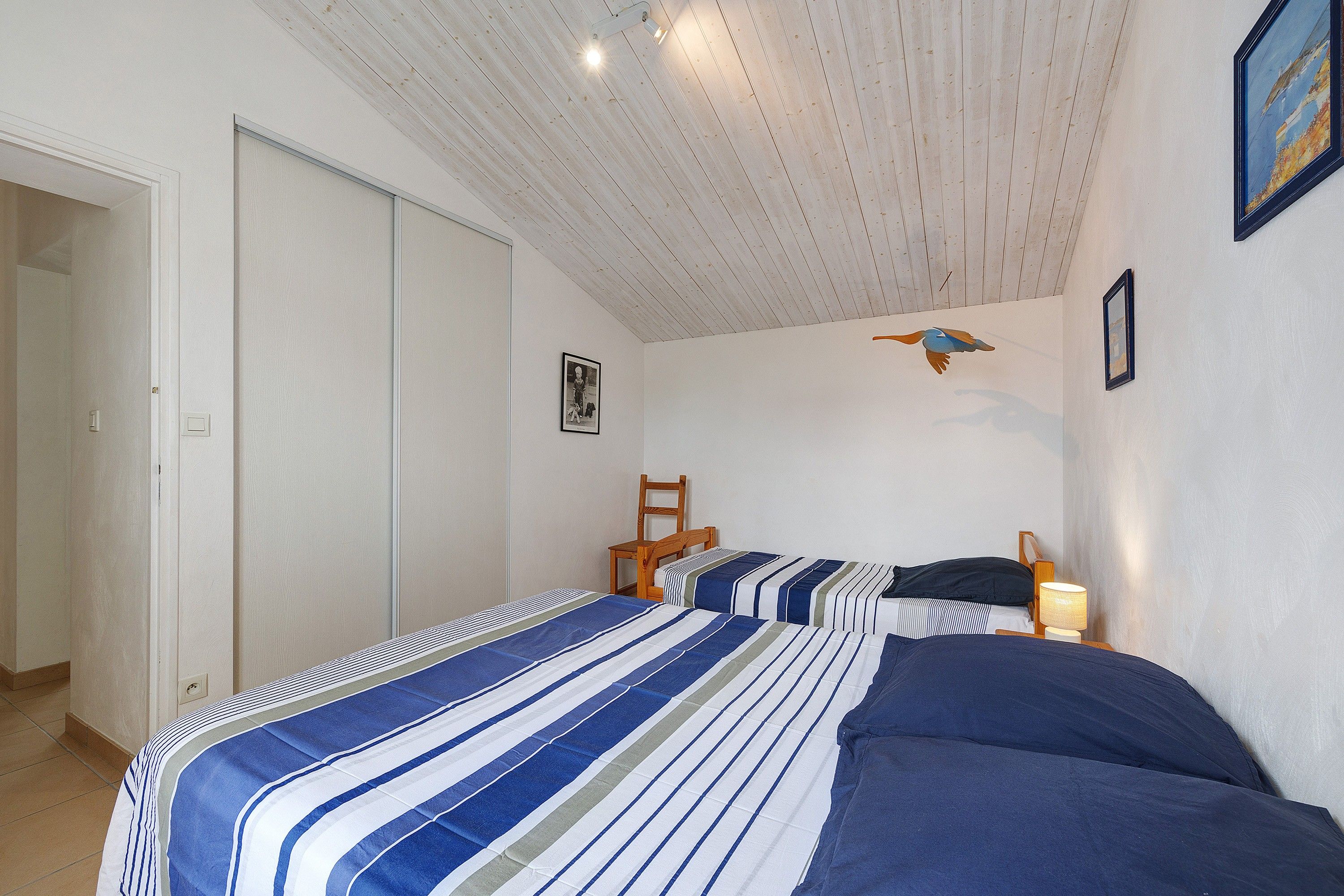 Ein Schlafzimmer mit zwei Betten, einer Holzbalkendecke, einem Sessel, einer Lampe und einem gerahmten Bild an der Wand.