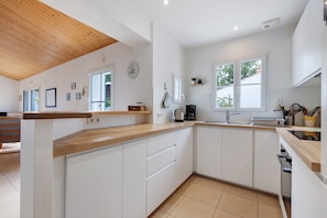 A modern kitchen with white cabinetry, a wooden countertop, and a visible clock on the wall.