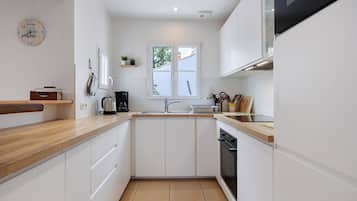 Une cuisine moderne avec des meubles blancs, un plan de travail en bois, un four encastré et une fenêtre donnant sur l’extérieur.