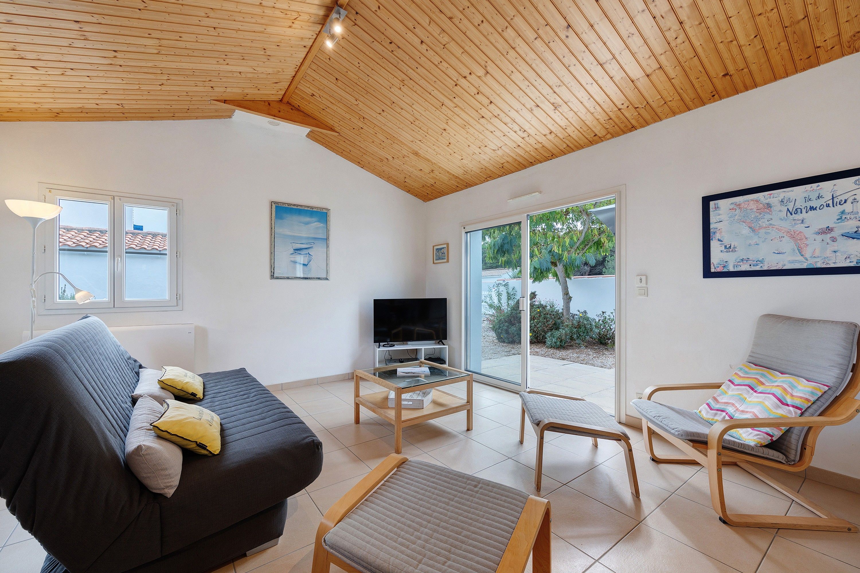 Una sala de estar moderna con techo de madera, un sofá, un televisor y una silla con un cojín colorido.