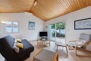 Una sala de estar moderna con techo de madera, un sofá, un televisor y una silla con un cojín colorido.