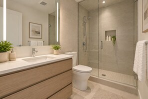 Un baño moderno con ducha envuelta en vidrio, un lavabo con tocador de madera y un inodoro.