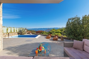 A poolside area with a view of mountains, a pool, lounge chairs, and a table with fruit and a drink. - Villa Bootshaus mit Pool und Meerblick (Vrbnik)
