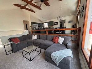 A modern living room with a sectional sofa, a glass coffee table, and a view of the kitchen and dining area. - Walk to Pool & Lake! 5BR Family Hideout Retreat With AC (Lake Ariel)