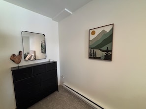Una habitación con un aparador negro, un espejo y un cuadro de paisaje en la pared.