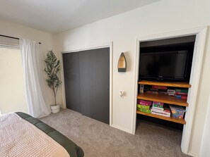A bedroom with a bed, a closet, a television, and a shelf with board games. - Walk to Pool & Lake! 5BR Family Hideout Retreat With AC (Lake Ariel)