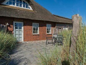 A brick building with a thatched roof, a sign reading 'Oland,' and a patio area with chairs and a table. - Holiday Apartment 1 "oland" (Tating)