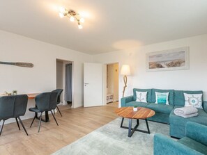 A modern living room with a teal sofa, two black chairs, a wooden coffee table, and a ceiling light fixture. - Apartment 6 "home Port" (St. Peter-Ording)