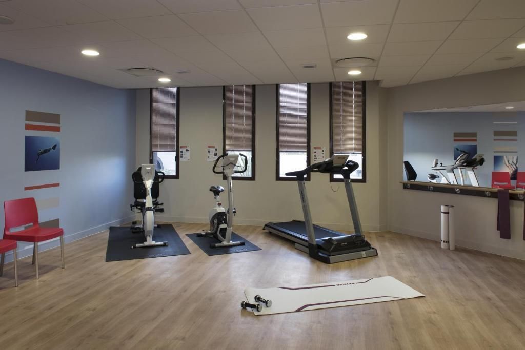 Une salle de sport équipée de matériel d’exercice, avec un fauteuil rouge et un grand miroir.