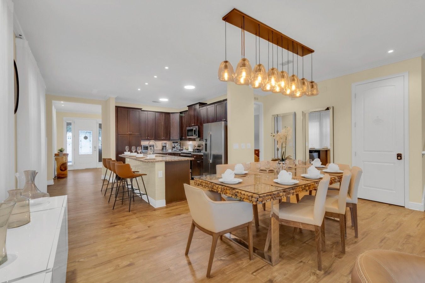 A modern kitchen with dark wood cabinets, a central island, and a dining area with a glass-top table and chairs.