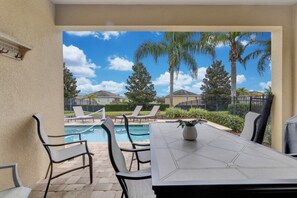A patio area with a pool, lounge chairs, and a table. - Themed 8BR Home w/ Private Pool & Custom Game Room (Kissimmee)