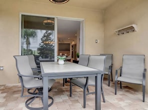 An outdoor patio with a table and chairs, a potted plant, and a view of the interior. - Themed 8BR Home w/ Private Pool & Custom Game Room (Kissimmee)