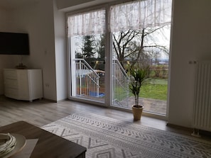 Una habitació amb una porta corredissa de vidre que dona a un balcó, un armari blanc, una catifa amb dibuixos i una planta en test.