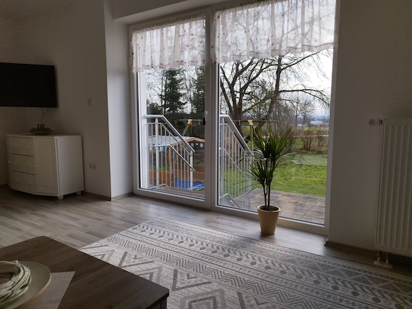 A room with a sliding glass door leading to a balcony, a white cabinet, a patterned rug, and a potted plant.