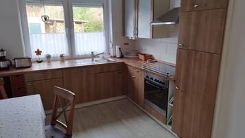 Een keuken met houten kastjes, een gootsteen, een fornuis en een raam met gordijnen.