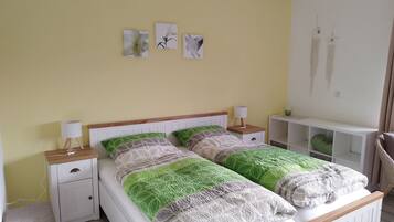 Een tweepersoonsbed met een houten hoofdbord, twee nachtkastjes met lampen, een witte bijzettafel, een groene kussen en een witte plankunit.