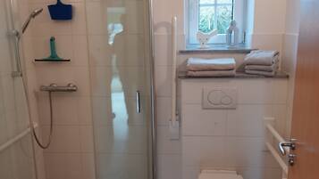 Een badkamer met een douchecabine van glas, een toilet, een wastafel en een raam met uitzicht op bomen.