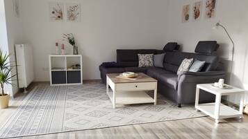 Een moderne woonkamer met een donkerbank, een witte salontafel, een witte bijzettafel, een kamerkleed met patroon en een radiator.