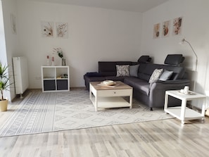 A modern living room with a dark-colored sofa, a white coffee table, a white side table, a patterned rug, and a radiator.