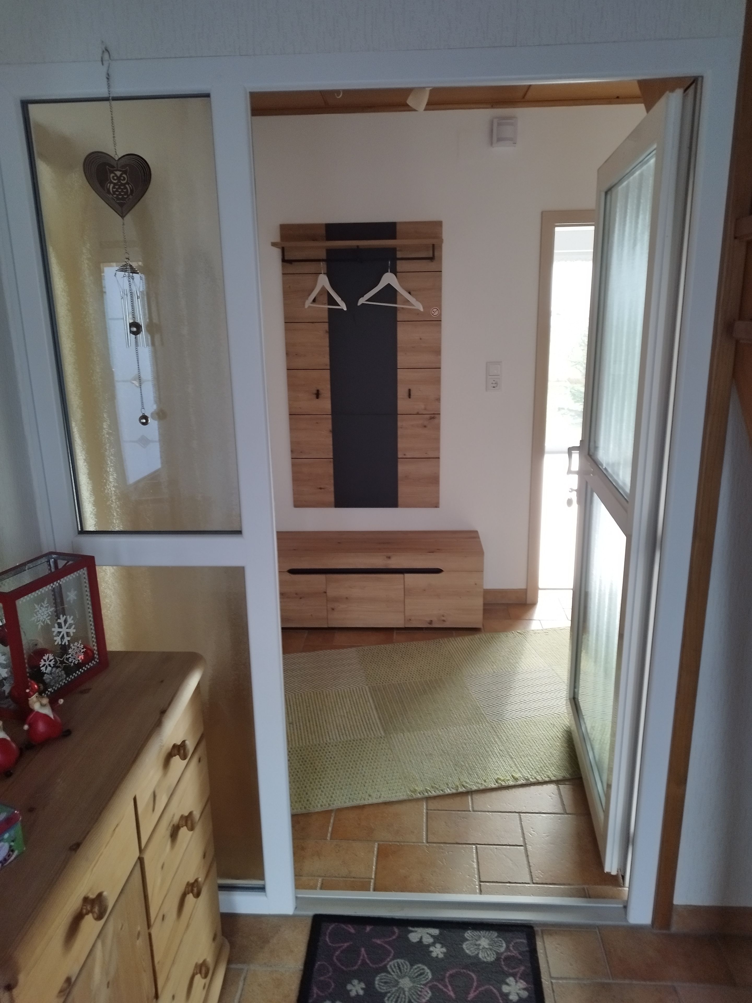 A room with a wooden dresser, a hanging ornament, and a door leading to another space.