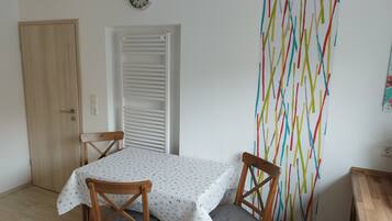 Een eetgedeelte met een tafel voor twee, een klok aan de muur en een kleurrijke abstracte wanddecoratie.