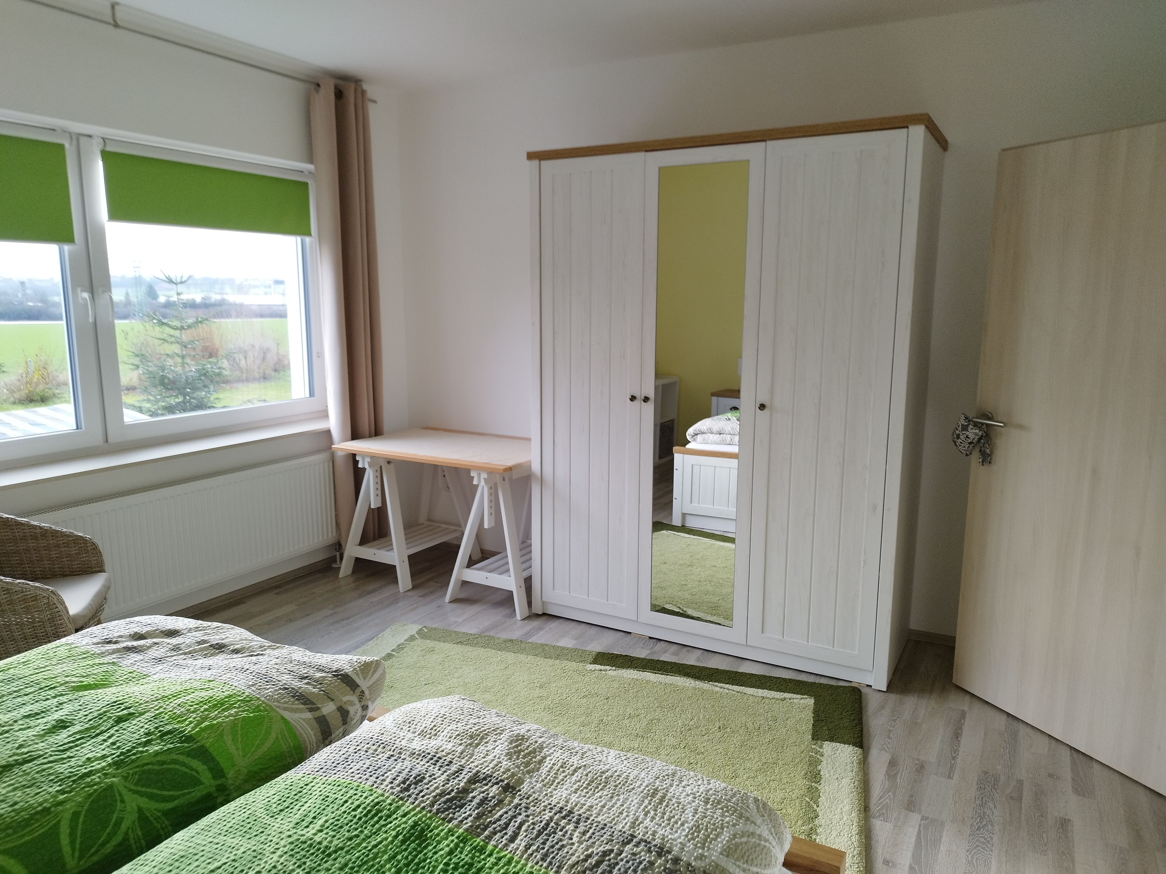 Ein Zimmer mit einem Bett, einem Schreibtisch, einem Kleiderschrank und einem Fenster mit Blick ins Freie.