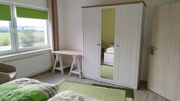 Ein Zimmer mit einem Bett, einem Schreibtisch, einem Kleiderschrank und einem Fenster mit Blick ins Freie.