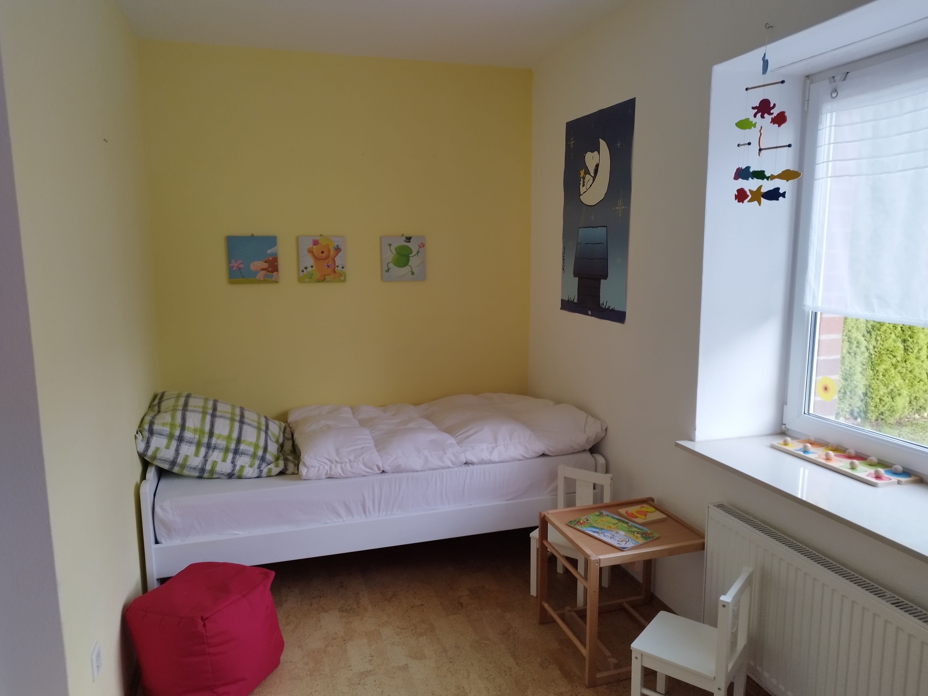 Ein Kinderzimmer mit einem Bett, einem kleinen Tisch, einem Stuhl und Wanddekorationen.