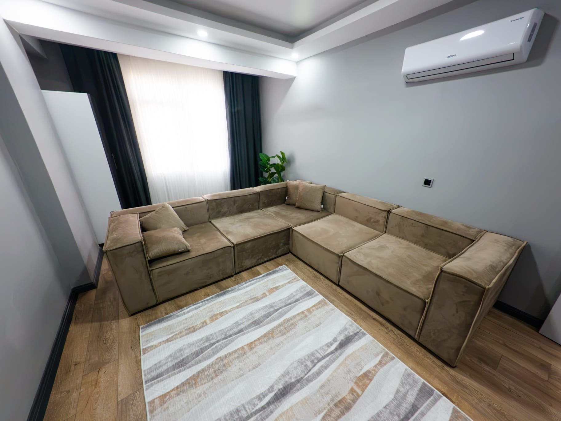 Una sala de estar moderna con un sofá modular, un tapete estampado y un equipo de aire acondicionado en la pared.