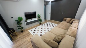 Uma sala de estar moderna com um sofá seccional bege, uma televisão de tela plana e duas plantas em vasos.