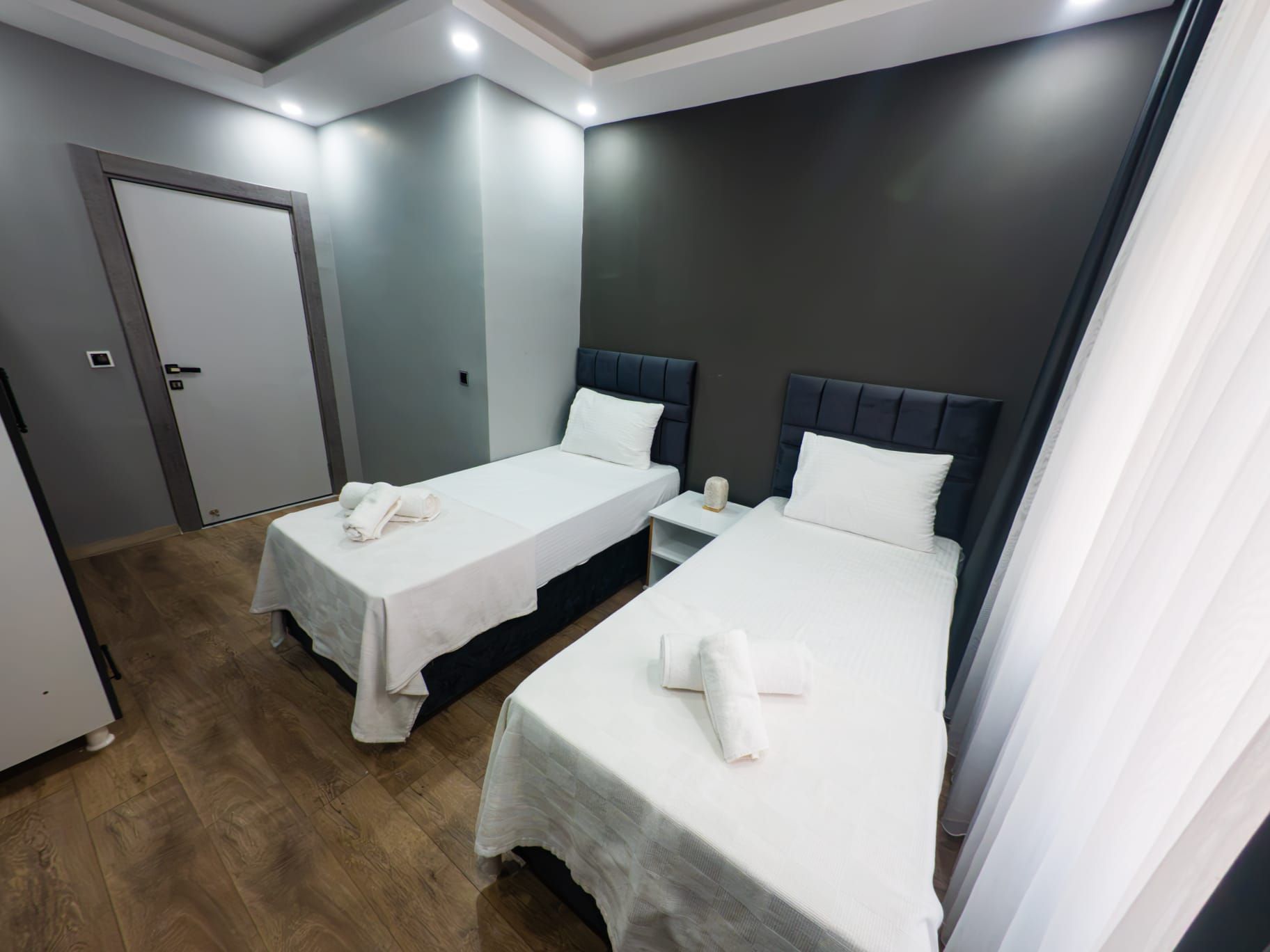 A hotel room with two single beds, a small table, and a door.
