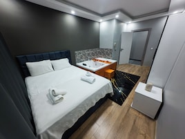 A modern hotel room with a large bed, a bathroom with a bathtub, and a wooden floor.