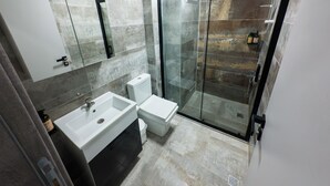 Un baño moderno con ducha envuelta en vidrio, un lavabo blanco y un inodoro.