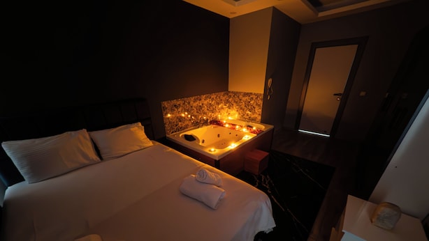 Habitación de hotel con una cama grande, una zona de estar con bañera y una puerta que da a otra habitación.