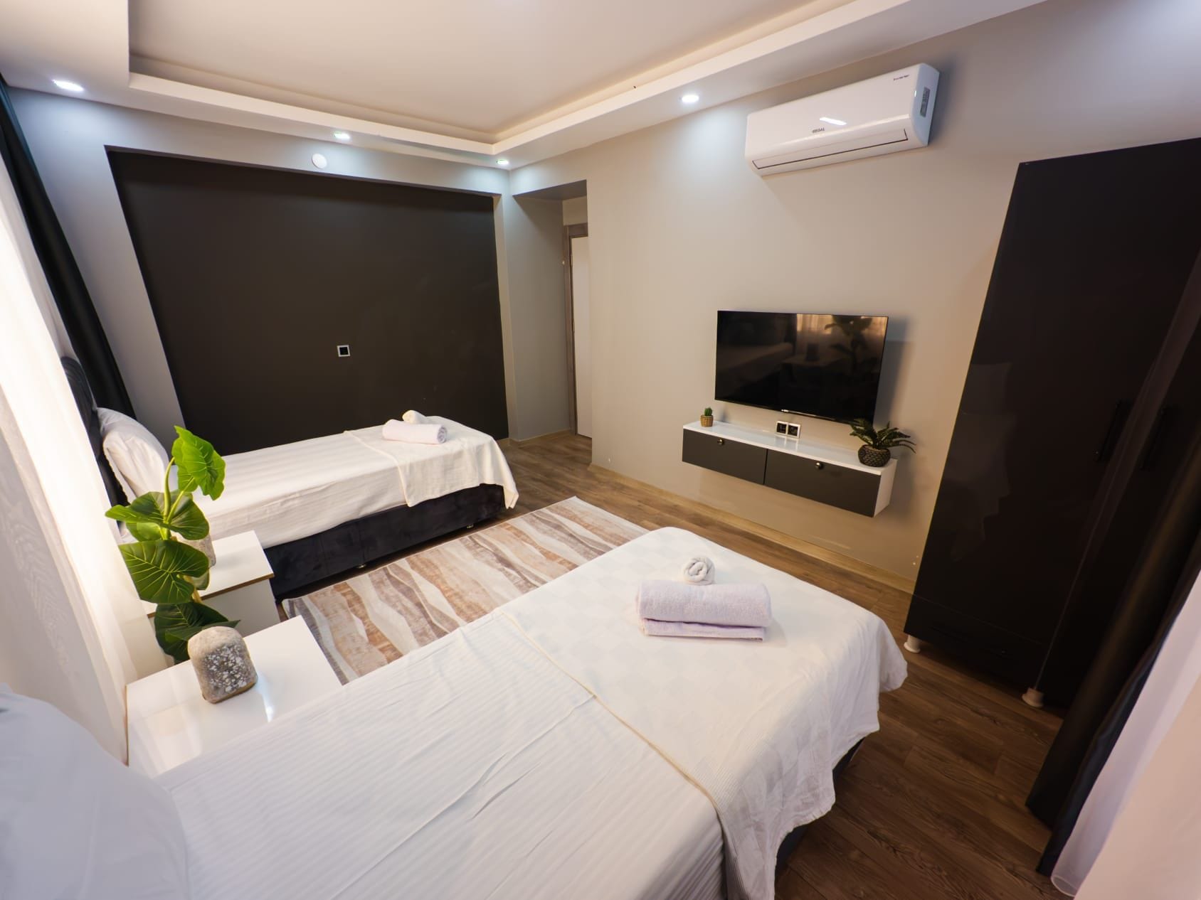 Et moderne hotelværelse med to senge, et fladskærms-tv, en lille plante og en indbygget aircondition.