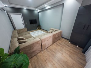 A modern living room with a sectional sofa, a flat-screen TV, and a dark-colored wardrobe.