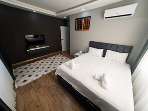 A modern hotel room with a bed, a flat-screen TV, an air conditioner, and a patterned rug.
