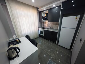 A compact kitchen with a white countertop, black cabinets, a built-in oven, and a refrigerator.