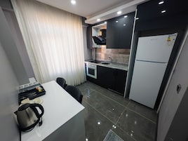 A compact kitchen with a white countertop, black cabinets, a built-in oven, and a refrigerator.