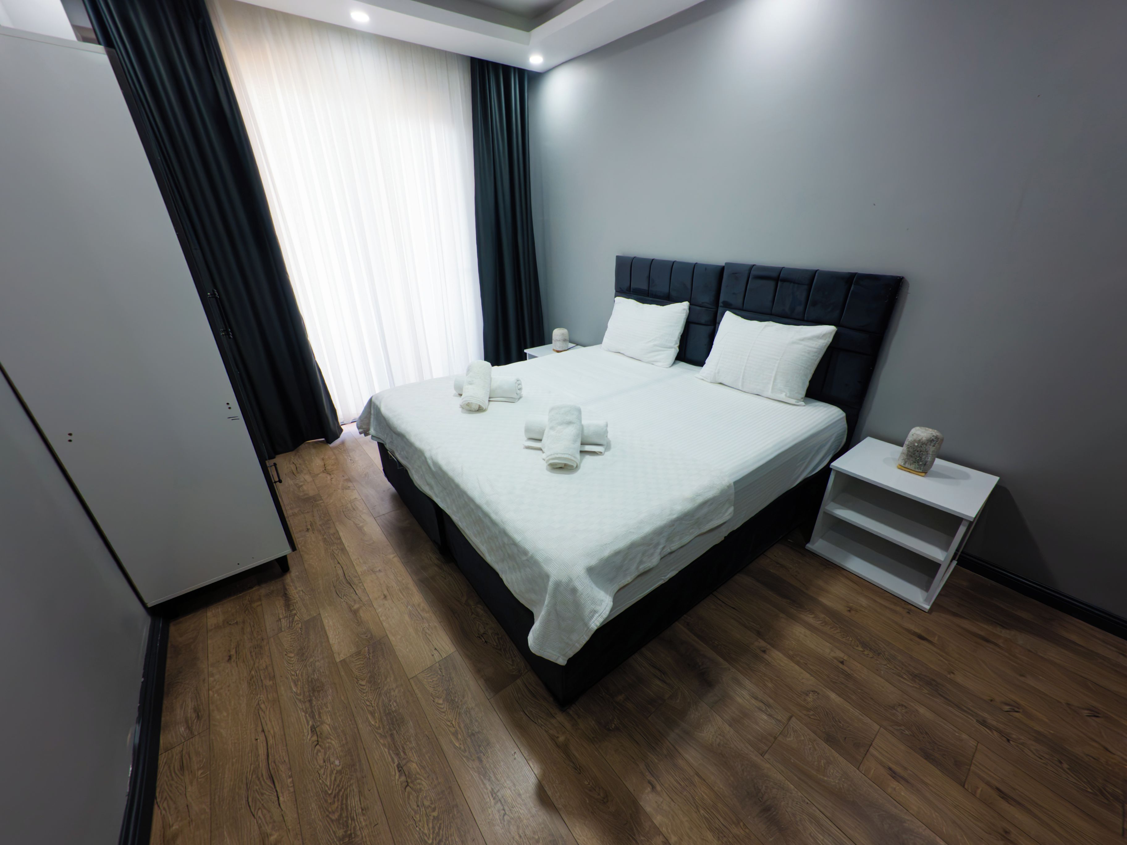 Ein ordentlich bezogenes Bett mit weißen Leinentüchern und Kissen, ein Nachttisch mit einer Lampe und ein Holzboden.