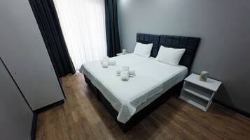 A neatly made bed with white linens and pillows, a bedside table with a lamp, and a wooden floor.